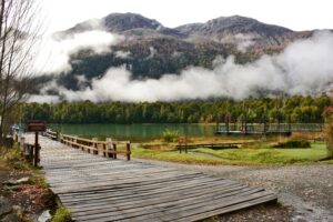 Tranquil scene of a mountain lake with a wooden dock and misty forests.